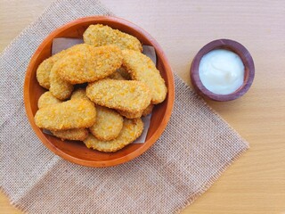 Fried chicken nuggets in a wooden plate and mayonnaise sauce in a small wooden bowl on a wooden table.