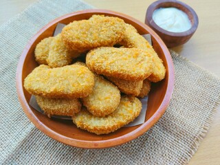 Fried chicken nuggets in a wooden plate and mayonnaise sauce in a small wooden bowl on a wooden table.