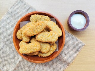 Fried chicken nuggets in a wooden plate and mayonnaise sauce in a small wooden bowl on a wooden table.
