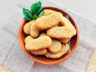 Fried chicken nuggets in a wooden plate on a wooden table.