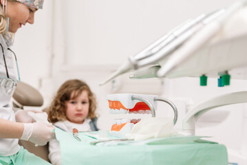 Female Dentist preparing tools and model of human jaw for examining little girl in dental clinic