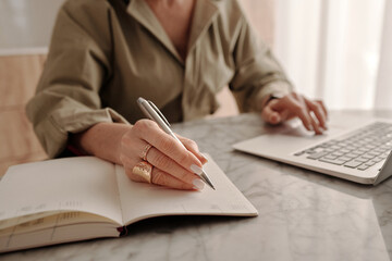 Medium section shot of unrecognizable middle-aged businesswoman sitting at table at home making notes in personal organizer