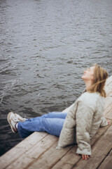 Fototapeta premium A young woman sits on a wooden pier against the background of a lake.