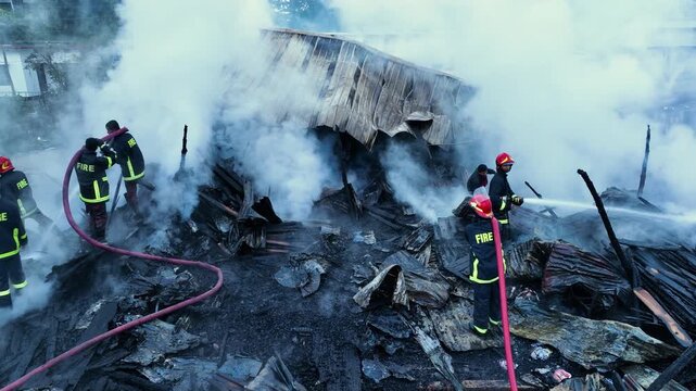 Khagrachari, Bangladesh - 20 August 2025: Aerial view of firefighters battling a blaze amidst thick plumes of smoke engulfing the charred remains of a building.