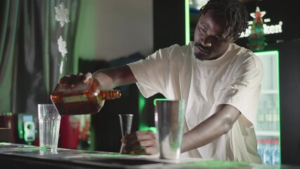 Bartender pouring whiskey from bottle into glass on bar counter in modern bar with green neon lighting, focused on drink creation, professional bartending skills