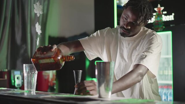 Bartender pouring whiskey from bottle into glass on bar counter in modern bar with green neon lighting, focused on drink creation, professional bartending skills