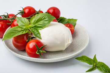 Fresh mozzarella cheese, cherry tomatoes and basil on plates on light background. Concept of Italian cuisine, capise salad and healthy eating.