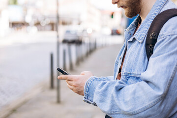 Man waiting at public transport stop using smartphone during daytime, copy space.