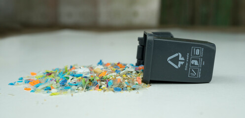 Microplastic granules spilled from a small bin, representing the global micro plastics pollution crisis and recycling challenges. Conceptual photo.