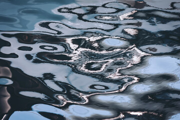 Rippling reflections dance across the tranquil surface of serene water under a soft golden sun, creating mesmerizing patterns at dusk in a hidden urban oasis