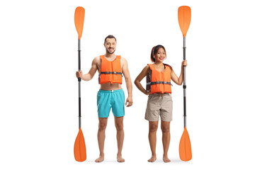 Full length portrait of a young man and woman wearing life jackets and holding paddles