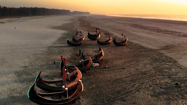 Cox's Bazar, Bangladesh - 20 August 2025: Aerial view of fishing boats resting on the expansive sandy beach during a golden sunset casting long shadows.