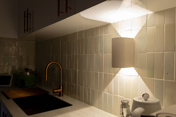 Under cabinet ceramic wall sconce casting upward and downward light on glossy tiled backsplash with...