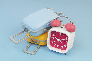 Red and white alarm clock with two suitcases on blue background.