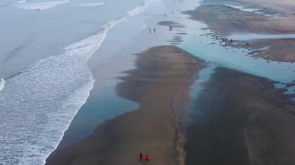 Cox's Bazar, Bangladesh - 20 August 2025: Aerial view of people walking on the beach, the waves crashing on the shore, and pools of water reflecting the sky.