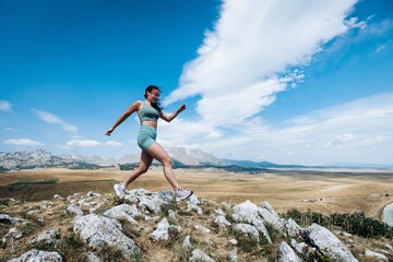 Woman running on rocky hill with scenic landscape.