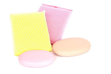 Colorful bath sponges with mesh texture and two oval soap bars placed on white background. Concept of body care, hygiene, spa, bathroom accessories, cleaning products, and healthy lifestyle.         
