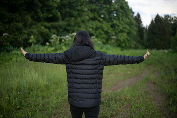 A girl in black clothes walks with her arms outstretched. A girl against the background of a forest. A girl in black clothes with black hair.