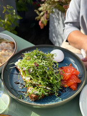 Breakfast pate with smoked salmon, poached Egg and Microgreens on a toast. Woman eat breakfast in cafe
