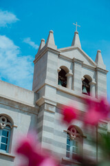 Stone Church Bell Tower with Cross and Pink Flowers – Blue Sky