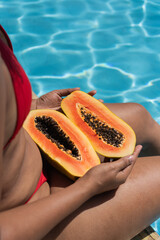 Woman holding papaya halves by the swimming pool