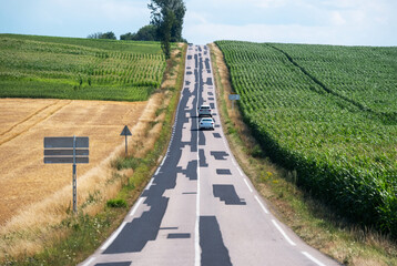A rural road stretches through fields, dominated by an unusual pattern of black asphalt repairs....
