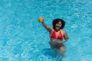 Young woman holding orange juice in swimming pool