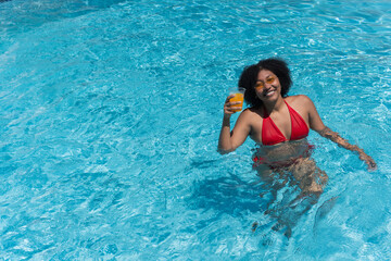 Young woman relaxing in swimming pool with tropical juice cocktail