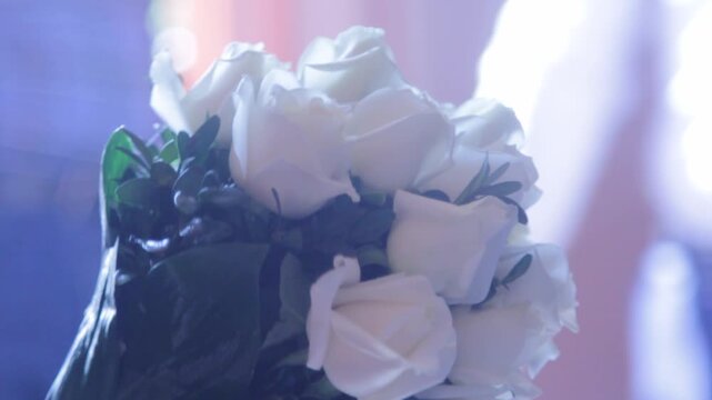 A stunning, multi-tiered wedding cake adorned with delicate pink flowers, displayed prominently at an elegant event with soft purple lighting and lush greenery.