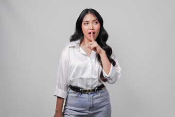 Pretty young Asian woman wearing white shirt gesturing silence or secret with her finger.