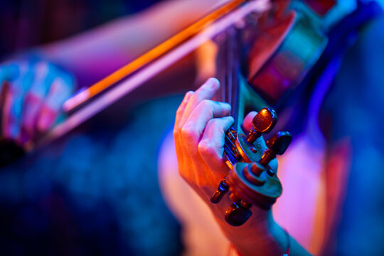 Close-up of woman hands playing violin under colorful stage lights