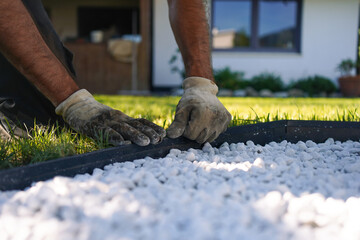 Garden worker's hands placing a Anthracite Metal Edge around a White Pebble Garden Bed