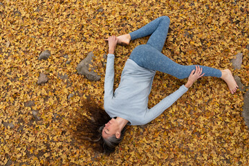 Woman practicing yoga on autumn leaves in reclining spinal twist position