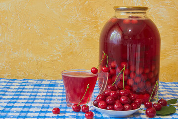 jar with cherry compote and fresh cherries on table, There is a large jar of cherry compote and a glass with a drink, as well as scattered red cherries on the table.