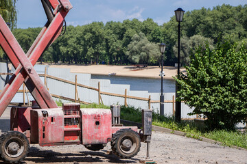Scissor lift near a riverbank with sandy beach and greenery on a sunny day