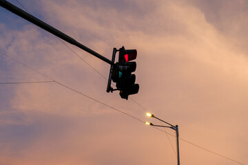 Red traffic light atop pole with sunset sky in urban setting