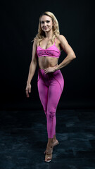 Fototapeta premium Athletic woman wearing pink sportswear showing her sculpted abs while posing on a black background 