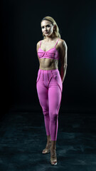 Athletic woman wearing pink sportswear showing her sculpted abs while posing on a black background
