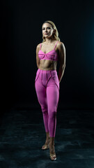 Athletic woman wearing pink sportswear showing her sculpted abs while posing on a black background
