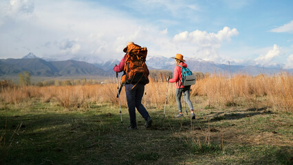Two travelers with backpacks walking at sunset. Two women are walking across a field towards the...