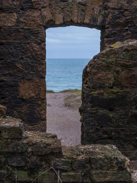 View of the rugged, stone window framing the ocean, beach, and sky, creating a stark contrast, Peterhead, Scotland, United Kingdom.