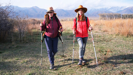 Two women have fallen behind their group of hikers and are walking alone through a field in the beautiful foothills. Hiking and trekking