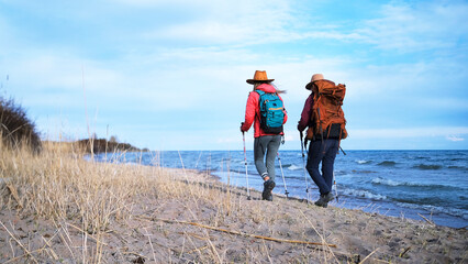 Back view of two travelers walking along the sea with backpacks. Lesbian couple strolling on the beach. The sisters are looking for camping