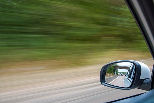 Traveling by car picture with motion blur from the window of a moving car. Focus on the wing mirror. Driving at speed. Automobile and transportation image.