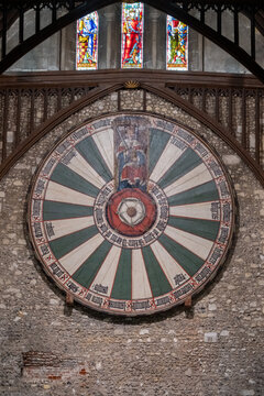 View of the legendary Round Table hanging majestically against the textured stone wall, illuminated by the vibrant stained-glass windows above, Winchester, England, United Kingdom.
