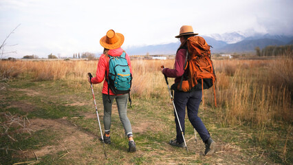Two young women take an active walk through a grassy field at sunset. Travelers enjoy nature and...