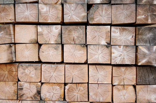 A folded bar in a stack. The end part is made of treated wooden beams. Background with a wood texture. Industrial texture of lumber. A close-up background image of a stack of wooden beams.