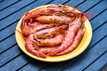 Pile of cooked red prawns on yellow plate, against a navy wood-grain table.