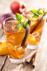 Refreshing peach iced tea in glass with ice cubes and cinnamon on wooden table
