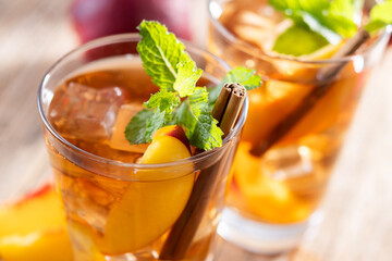 Refreshing peach iced tea in glass with ice cubes and cinnamon on wooden table